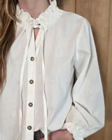 Camisa de manga larga con estampado de cuadros en tonos azules y rojizos. Presenta un cuello alto con volados y puños elásticos con detalle de volado en el extremo. Cierre frontal con botones ocultos.