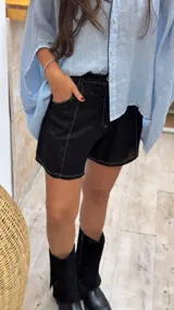 Short de lino color negro con costuras a la vista en color blanco que resaltan el diseño. Presenta un corte clásico con bolsillos laterales y cierre frontal.