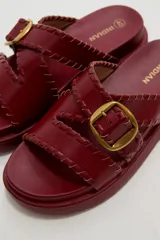 Sandalias planas de eco cuero color bordó, con tiras cruzadas y hebilla metálica dorada.