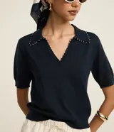 Blusa negra de punto con cuello polo, escote en V y mangas cortas. Detalle de mini perlas aplicadas en el cuello.