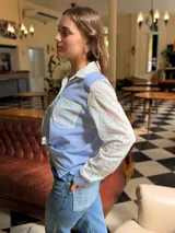 Camisa de corte clásico con diseño combinado, presenta cuerpo a rayas verticales en azul y blanco, con mangas largas y cuello en tela broderie blanca con detalles calados. Incluye bolsillo frontal en broderie y cierre central con botones.