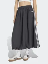 Falda larga de estilo deportivo con silueta voluminosa tipo globo, confeccionada en tejido técnico color negro. Presenta el diseño clásico de tres rayas blancas laterales y el logo del trébol bordado. Cuenta con cintura elástica y cierre lateral.