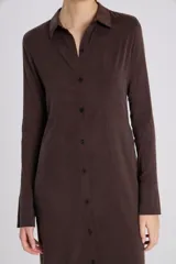 Vestido camisero largo color rojo oscuro, de manga larga y cuello camisero. Presenta un cierre frontal completo con botones oscuros y una abertura en el ruedo.