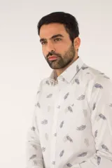 Camisa de manga larga con corte slim fit, color blanco con estampado de hojas pequeñas en tonos grises y azules. Presenta cuello clásico, cierre frontal con botones y logo bordado en el pecho.
