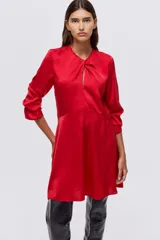 Vestido corto de color rojo, con escote redondo y detalle girado en el frente. Presenta mangas largas con abertura en los puños, falda con leve vuelo y cierre oculto en la espalda.