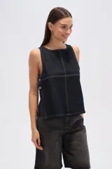 Musculosa de jean azul oscuro, de corte holgado, con cuello bote, pespuntes blancos y cierre lateral con botones metálicos.