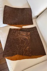 Minifalda marrón de cuero ovino con textura veteada y detalle de ojales metálicos.