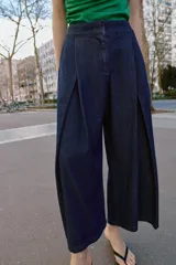 Pantalón tipo culotte de tiro alto confeccionado en denim azul oscuro. Presenta pinzas delanteras, pernera ancha y corta, bolsillos laterales ocultos y cierre frontal con cremallera, botón y ganchos.