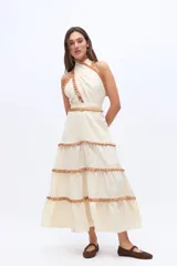 Vestido midi de lino color beige, con diseño de cuello halter cruzado y detalles de volados en tono marrón en el cuello, cintura y los niveles de la falda.