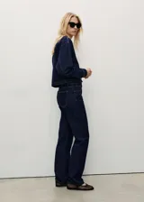 Pantalón de jean de corte recto y tiro medio, en color azul oscuro con costuras en contraste. Presenta diseño clásico de cinco bolsillos, cierre frontal con cremallera y botón, y trabillas para cinturón.