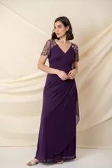 Vestido largo de fiesta color violeta, con cuerpo de jersey y falda de gasa con diseño drapeado y sobrecapa. Presenta escote en V y mangas cortas de tul bordado con pedrería al tono.