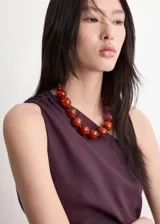 Vestido midi color marrón, de diseño asimétrico con un solo hombro descubierto, detalle fruncido en el lateral y abertura en el bajo.