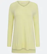 Blusa de punto color amarillo claro, con escote en V, mangas largas con textura acanalada y diseño de ruedo asimétrico tipo mullet con aberturas laterales.