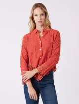 Camisa de algodón con bordado suizo, cuello con solapa y cierre frontal con botones. Presenta mangas largas con terminación de encaje calado y un ruedo asimétrico en pico con un amplio galón de encaje.