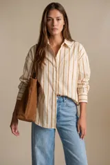 Camisa de corte oversize con estampado de rayas verticales en tonos beige y mostaza. Presenta cuello clásico, cierre frontal con botones, bolsillo aplicado en el pecho y mangas largas con puños abotonados.