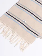 Bufanda de tejido suave en color marrón chocolate con diseño de rayas horizontales en tonos naranja, beige y gris. Presenta terminaciones con flecos en los extremos.
