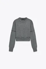 Jersey de punto gris oscuro, cuello redondo y manga larga. Presenta detalles desmontables con botones a lo largo de las costuras de las mangas y en el ruedo inferior.