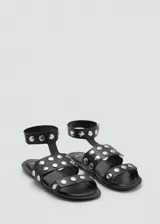 Sandalia plana de cuero negro con punta cuadrada, doble tira frontal y tira tobillera, decoradas con tachuelas metálicas plateadas.