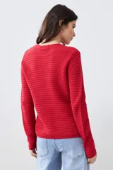 Chaqueta de punto color rojo, de corte entallado y manga larga. Presenta cuello redondo y cierre frontal con botones metálicos dorados texturizados.