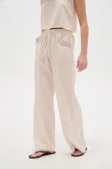 Pantalón ancho de viscosa color beige claro, de tiro alto con cintura elastizada y cordón ajustable. Presenta bolsillos laterales decorados con detalles bordados geométricos.