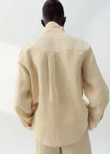 Camisa de lino color beige, de diseño recto con cuello camisero, manga larga con puños abotonados, bolsillo de parche en el pecho y cierre frontal de botones.
