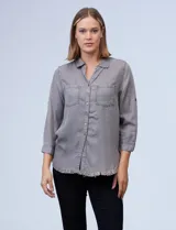 Camisa gris de tencel con cuello con solapa, escote en V y abertura central con botones. Delantera con bolsillos, mangas 3/4 regulables con presilla y botón, y ruedo desflecado.