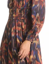 Vestido midi de manga larga con escote en V, confeccionado en tela fluida con estampado abstracto multicolor. Presenta una cintura elástica fruncida que define la silueta y una falda con caída suave y movimiento.