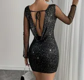 Vestido corto de fiesta color negro con acabado brillante tipo glitter. Presenta mangas largas de tul transparente, escote profundo en la espalda con detalle de lazo ajustable y corte ajustado al cuerpo.