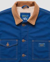 Campera estilo workwear de Denali, confeccionada en canvas resistente color azul royal. Cuenta con interior forrado en corderito sherpa, cuello de pana en color tostado, cierre frontal con botones metálicos color cobre y cuatro bolsillos frontales.