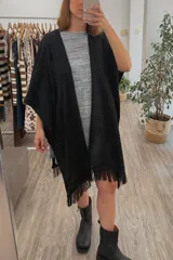 Ruana tejida color negro con diseño calado y flecos en los bordes.