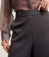 Pantalón de sastrería de corte recto y tiro alto, con diseño de pierna ancha, trabillas en la cintura, cierre frontal con botón y cremallera, y bolsillos laterales con costuras verticales.