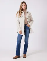 Sobrecamisa de corte amplio confeccionada en tejido suave al tacto, color beige. Presenta cuello de solapa, cierre frontal con botones efecto carey, dos bolsillos frontales con solapa y mangas largas con puños abotonados. El ruedo es redondeado en los laterales y cuenta con canesú en la espalda.