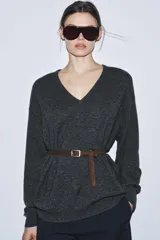 Jersey oversize de lana con escote en pico y manga larga. Incluye un cinturón fino de cuero en tono marrón con hebilla metálica dorada.