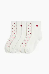 Pack de cinco pares de medias de caña media color blanco, confeccionadas en punto fino de mezcla de algodón. Tres pares tienen un estampado de pequeños corazones rojos distribuidos por toda la media, y dos pares son lisos, con un corazón rojo bordado en la parte superior.