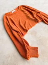 Buzo de tejido de punto con acabado brillante, confeccionado con hilado italiano. Presenta cuello redondo, mangas largas acampanadas y un corte holgado.