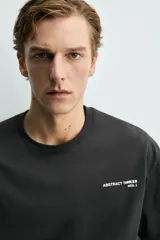 Camiseta de corte boxy fit, color negro, con cuello redondo y manga corta. Presenta estampados a contraste en el pecho y en la espalda.
