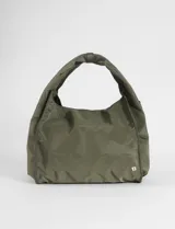 Cartera tipo shopper de tamaño grande, color verde militar, con diseño de asa única integrada y detalle de logo metálico pequeño en la esquina inferior.