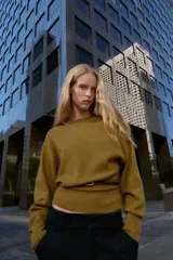 Jersey de punto color mostaza con cuello barco, manga larga con sisa ancha y detalle de cinturón fino integrado en la cintura.