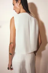 Chaleco blanco de cuello redondo y sin mangas, con cierre frontal cruzado con un botón.