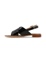 Sandalia de cuero charol negro con tiras anchas cruzadas en el empeine y tira trasera con hebilla metálica ajustable. Cuenta con suela plana y taco bajo de madera.
