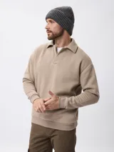 Sweater de felpa color beige, con cuello polo y cierre frontal parcial, de manga larga con puños acanalados.