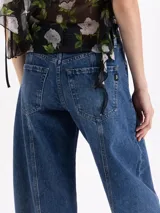 Jeans de tiro medio con silueta slouchy y corte amplio. Presenta recortes verticales que estructuran la prenda, generando volumen desde el muslo hasta la bota. Confeccionado en denim de lavado clásico con desgastes localizados.