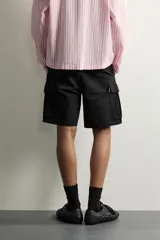 Bermuda cargo color negro de corte relaxed fit, confeccionada en tejido de algodón con elasticidad y efecto lavado. Cuenta con cintura elástica ajustable con cordón, bolsillos frontales y bolsillos laterales tipo cargo con solapa en las perneras.