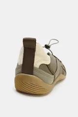 Zapato tipo bailarina deportiva color verde oliva con detalles en beige claro. Presenta cuerpo con contraste de materiales, sistema de ajuste elástico con tope fruncidor y suela de goma color caramelo.