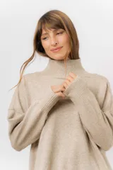 Sweater de tejido de punto color beige, con cuello alto, hombros caídos, mangas largas con puños acanalados y tajos laterales en el ruedo.