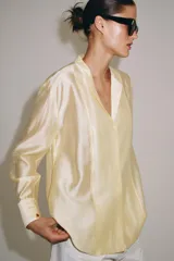 Camisa de mujer fluida de ZARA WOMAN COLLECTION, confeccionada en hilatura con mezcla de lyocell. Presenta escote en pico, manga larga con puños marcados y bajo asimétrico, con cierre frontal de botones ocultos.