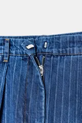 Pantalón de denim azul con rayas blancas verticales, tiro medio y corte balloon holgado. Presenta pliegues frontales, bolsillos laterales y falsos bolsillos de vivo en la espalda.