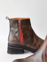 Botas cortas de cuero color chocolate, con elástico lateral, cierre interno con cremallera roja, pespuntes rojos y suela track.