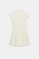Vestido mini satinado de color blanco, con escote en V pronunciado, mangas cortas casquillo y detalles de botones revestidos en el frente con presillas. Presenta un diseño ajustado en la cintura con costuras estilo corsé y falda corta con vuelo terminada en volante.