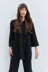 Cardigan negro de punto con acabado brillante, cuello redondo, cierre frontal de botones y detalle de cordones laterales entrelazados. Presenta mangas tres cuartos con diseño acampanado.